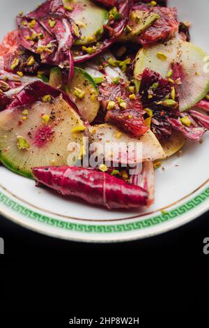 Radicchio Salat mit Wassermelone Rettich, Blutorange, Pistazien auf weißem Teller mit grünem griechischen Schlüssel Stockfoto