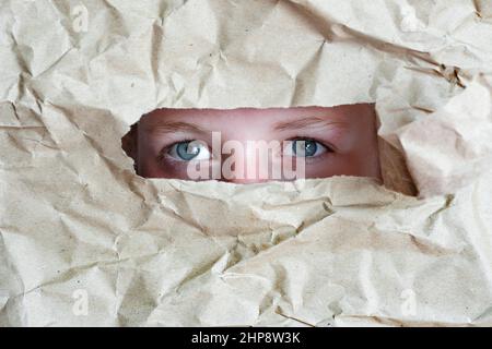 Weibliche Augen sehen Loch in einem zerknittert Papier Hintergrund. Frau, die aus dem Loch in das Papier guckt Stockfoto