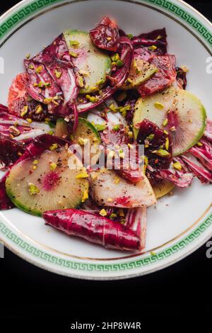 Radicchio Salat mit Wassermelone Rettich, Blutorange, Pistazien auf weißem Teller mit grünem griechischen Schlüssel Stockfoto