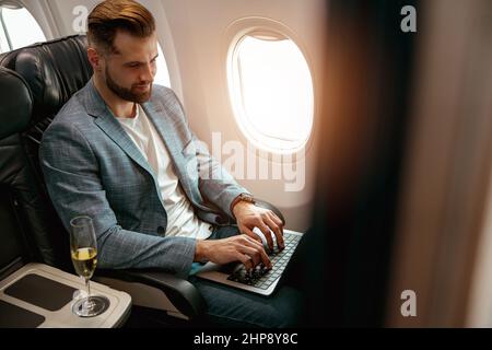Bärtiger Mann, der im Flugzeug am Laptop arbeitet Stockfoto