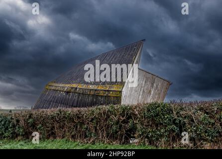 Ein Gebäude aus einem hölzernen Pferdestall, das bei extremen starken Winden auf seine Seite geblasen wurde, stürmt Donner den dunklen Wolkenhimmel Stockfoto