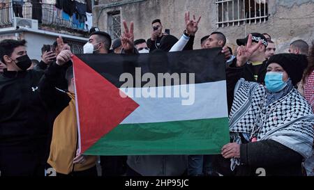 Palästinenser halten das Siegeszeichen und die palästinensische Flagge hoch, während einer Demonstration gegen israelische Besatzung und Siedlungsaktivitäten im Stadtteil Sheikh Jarrah am 18. Februar 2022 in Jerusalem, Israel. Das palästinensische Viertel Sheikh Jarrah ist derzeit das Zentrum einer Reihe von Eigentumsstreitigkeiten zwischen Palästinensern und rechtsgerichteten jüdischen Israelis. Einige Häuser wurden nach einem Gerichtsurteil von israelischen Siedlern besetzt. Stockfoto