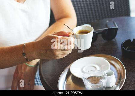 Frau trinkt heißen Kaffee im Café im Freien, Frau sitzt im Restaurant und hält eine Tasse Espresso Stockfoto