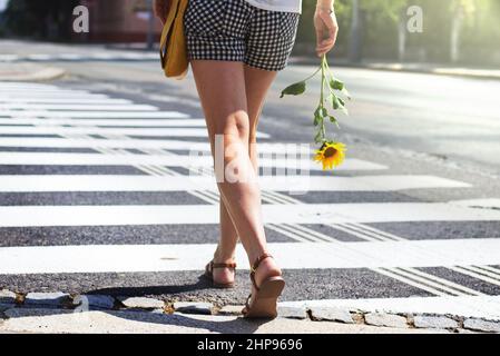 Weibliche Beine an der Fußgängerüberfahrt. Frau, die auf einem Fußgängerüberweg die Straße überquert, Sommer in der Stadt Stockfoto