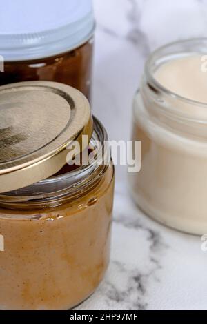 Vertikale Aufnahme von drei Gläsern mit Deckeln, die mit verschiedenen Cremes und Buttersorten auf dem Tisch gefüllt sind Stockfoto