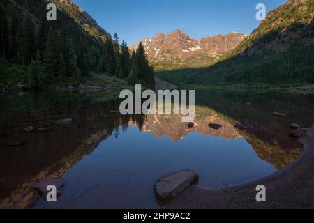 Maroon Bells, kristallklarer Maroon Lake und wunderschöne Sommerreflexionen am frühen Morgen in der Nähe von Aspen, Colorado Stockfoto