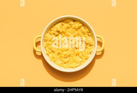 Oben mit einer Portion Rührei in einer Emaille-Platte isoliert auf einem orangen Hintergrund. Rühreier Teller minimalistisch auf einem bunten Tisch. Stockfoto