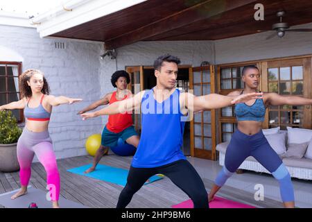 Junge biracial männliche und weibliche Freunde üben Krieger Pose zusammen auf der Terrasse Stockfoto