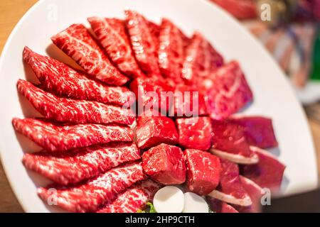 Nahaufnahme von gefälschten Kunststoffplatten vor dem Restaurant mit rotem rohem Fleisch, japanischem kobe oder Wagyu-Rindfleischschnitten, die hinter Glasfenster in Tok geschnitten wurden Stockfoto