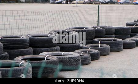 Sicherheitsbarriere aus alten schwarzen Reifen, die auf einem Betonpflaster hinter dem grünen Gitterzaun liegen. Viele befestigte Autoreifen für die Herstellung einer Spur barri verwendet Stockfoto