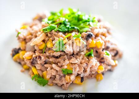 Makro-Nahaufnahme von cremigem Reis und schwarzer Bohnenschale mit Koriander und Maisgemüse als gesunde Mahlzeit auf weißem Teller, der Textur und Details zeigt Stockfoto