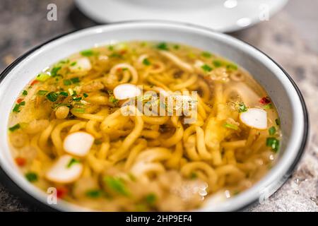 Makro-Nahaufnahme der japanischen udon Ramen Nudelsuppe in Schüssel als asiatische Mahlzeit mit Textur von Belag schwimmenden wie Fischkuchen und grüne Zwiebel Stockfoto