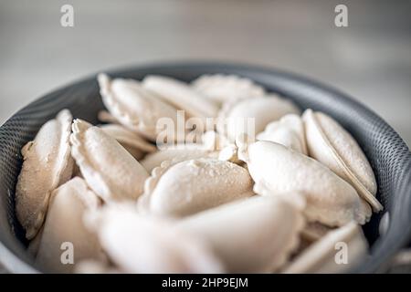 Kochtopf mit gefrorenen traditionellen russischen Knödel Vareniki oder polnischen Pierogi gefüllt mit Kartoffeln oder Käse zum Kochen Nahaufbereitungsmakro Stockfoto