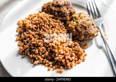 Burger Fleischbällchen mit Hackfleisch und traditionellen russischen Buchweizen gekochte Körner auf weißem Teller und Gabel Makro Nahaufnahme oben Stockfoto