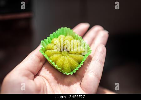 Nahaufnahme Makro der Hand hält grünen Tee Matcha oder Melone gefüllt Mochi Reiskuchen japanischen Dessert mit Papierverpackung als Snack Dessert Stockfoto