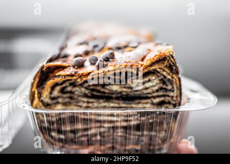 Gebackenes jüdisches Babka-Gebäck aus Schokoladenstückchen und Challah-Brotteig in einem Kunststoffpackungsladen mit Querschnittsansicht der geschnittenen Schichten Stockfoto