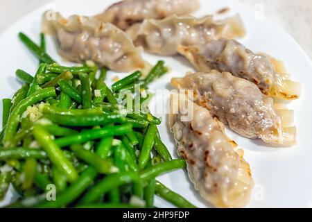 Japanisches oder koreanisches Rindfleisch Gyoza oder Mandu auf weißem Teller mit grünen Bohnen Makro-Nahaufnahme von asiatischen Speiseknödeln Stockfoto