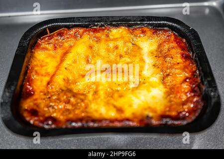 Italienische Fleisch Lasagne Paket gefroren tv-Esstablett im Ofen oder Mikrowelle mit geschmolzenem Käse und schwarzem Kunststoffbehälter gebacken Stockfoto