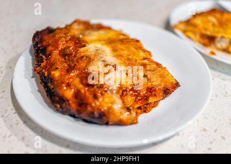 Italienische Fleischlasagne im Ofen gebacken mit geschmolzenem Käse und Kruste auf weißem Teller zum Abendessen mit Textur Makro-Nahaufnahme der roten Marinara-Sauce Stockfoto