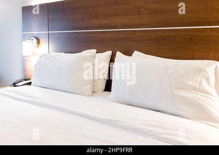 Das Schlafzimmer war leer, mit einer beleuchteten Lampe und einer Nahaufnahme von vier weißen Kissen mit Laken auf dem Kopfteil des Matratzenbettes in einem modernen Hotel, in dem niemand war Stockfoto