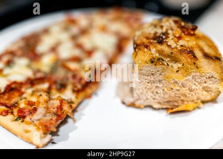 Eine halbe dünne, gefrorene oder hausgemachte Pizza mit Gemüseüberzug und sonnengetrocknetem Tomatenfoccacia-Brot auf weißem Teller Makro-Nahaufnahme Stockfoto