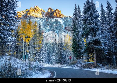 Maroon Bells Creek Road in Aspen, Colorado Felsenberge, die nach dem Winter-Spätfall mit Schneefall bedeckt sind, mit Sonnenlicht auf der Spitze und dunklem Waldgelb Stockfoto