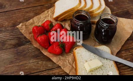 Sandwiches oder Toast mit Butter. Erdbeer- und Konfitüren-Gläser auf Holztisch. Frühstück und Happy-Morning-Konzept Stockfoto