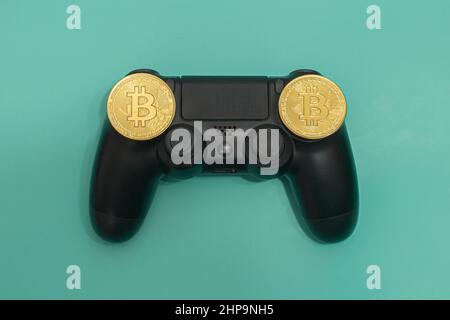 Schwarzer Gaming-Controller mit Bitcoin-Token auf grünem Hintergrund isoliert. Stockfoto