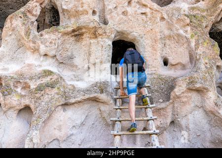 Mann klettert im Sommer auf dem Main Loop Trail im Bandeler National Monument in New Mexico eine Leiter hinauf auf die Klippe der Schlucht, um dort in einer Höhle zu wohnen, die von einheimischen p Stockfoto