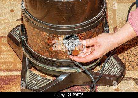 Der Prozess der Reinigung des Teppichs mit einem Staubsauger mit einem Wasserfilter. Die Hand einer Frau öffnet ein Loch, um Luft in einen Staubsauger zu blasen. Stockfoto