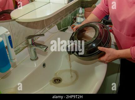 Der Prozess der Reinigung des Teppichs mit einem Staubsauger mit einem Wasserfilter. Eine Frau gießt nach dem Reinigen schmutziges Wasser aus einem Staubsaugertank. Stockfoto