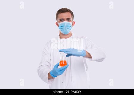 Männlicher Arzt zeigt Flasche mit farbiger Flüssigkeit tragen medizinische Maske, Handschuhe isoliert. Wissenschaft, Medizin, Virenkonzept. Mann, Doktor, Grillend. Flüssigkeit Stockfoto