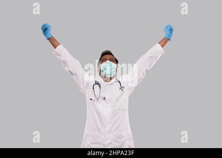Arzt begeistert Hände hoch Erfolg zu feiern tragen medizinische Maske und Handschuhe isoliert. Indischer Mann Arzt Glücklich Stockfoto