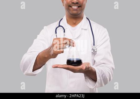 Männlich Arzt zeigt Flasche mit Colorfull Flüssigkeit isoliert Nahaufnahme. Wissenschaft, Medizin, Virenkonzept. Indischer Mann Arzt Schmillend. Stockfoto