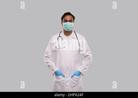 Arzt trägt medizinische Maske und Handschuhe stehen isoliert. Indischer Mann Arzt Medizinische Arbeitskleidung. Medizinisches Konzept Stockfoto