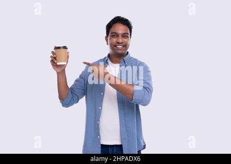 indischer Mann hält Kaffee zu gehen Tasse zeigt auf sie. Indian man mit Kaffee Take Away Tasse in der Hand. Isoliert Stockfoto