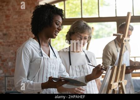 Glückliche junge afroamerikanische Frau, die mit einem alten Lehrer zeichnet. Stockfoto