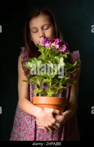 Schönes kleines Mädchen mit königlichem Pelargonium in den Händen Stockfoto