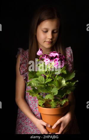 Schönes kleines Mädchen mit königlichem Pelargonium in den Händen Stockfoto