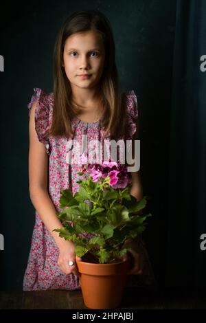 Schönes kleines Mädchen mit königlichem Pelargonium in den Händen Stockfoto