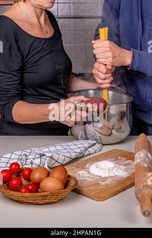 Ein Mann steckt Spaghetti in einen Topf mit kochendem Wasser, das eine Frau in ihrer Hand hält Stockfoto