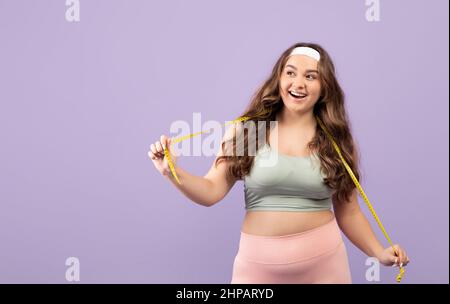 Froh überrascht plus Größe europäische junge Frau in Sportbekleidung mit Maßband und offenem Mund Stockfoto