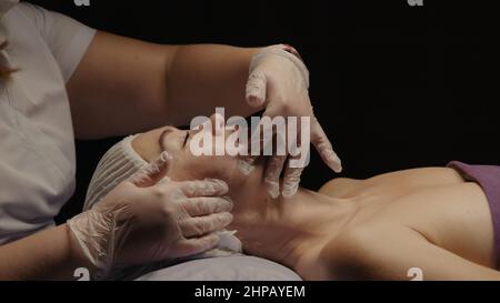 Junge hypnotische Gesichtsfrau erhält Anti-Aging-Gesichtsmassage im Spa-Salon Relax. Wellness Körper Hautpflege Gesicht Schönheitsbehandlung, Verjüngungskur bekommen Kopf Gesichtsmassage. Schwarzer Hintergrund Stockfoto