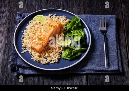 Portion pochierter Lachs in Kokos-Limetten-Sauce mit braunem Reis und frischem Spinat, Lachsfisch-Limettengericht mit Reis und Gemüse auf einem Teller, Blick von oben Stockfoto