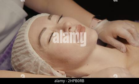 Junge hypnotische Gesichtsfrau erhält Anti-Aging-Gesichtsmassage im Spa-Salon Relax. Wellness Körper Hautpflege Gesicht Schönheitsbehandlung, Verjüngungskur bekommen Kopf Gesichtsmassage. Schwarzer Hintergrund Stockfoto