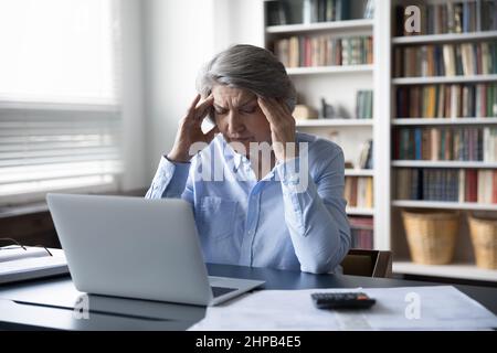 Erschöpfte, unglückliche Frau mittleren Alters, die an Kopfschmerzen leidet. Stockfoto