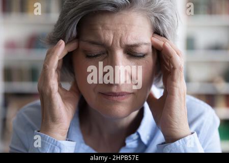 Gestresste unglückliche ältere Frau mit starken Kopfschmerzen. Stockfoto