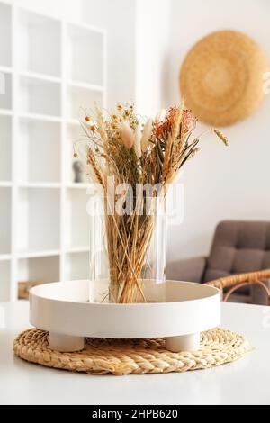 Vase mit getrockneten Blumen und Tablett auf weißem Tisch im Esszimmer Stockfoto