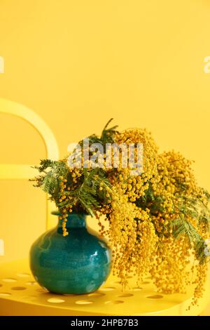 Vase mit Mimosenblumen auf Stuhl in der Nähe der gelben Wand Stockfoto