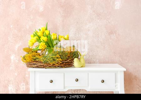 Nest mit schönen Blumen und Ostern Dekor auf dem Tisch neben Farbwand Stockfoto